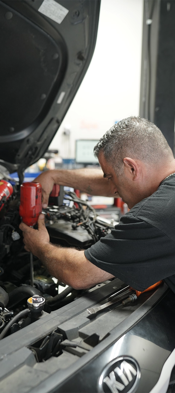 Mechanic Using Power Tool for Auto Repair Under Open Car Hood