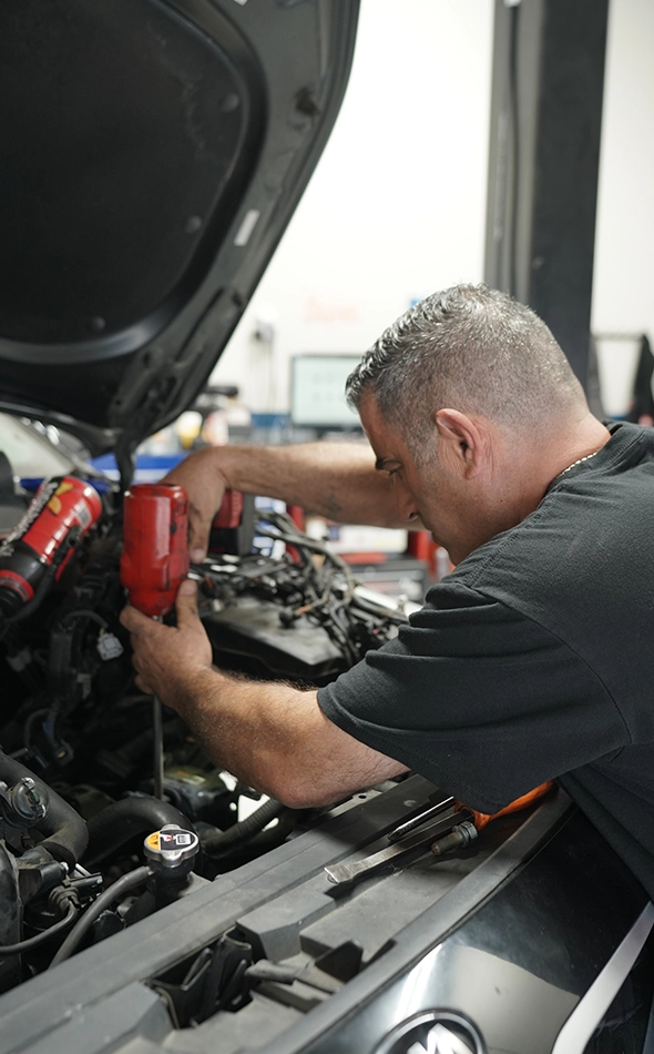 Mechanic Performing Auto Repair Under Car Hood in Shop Near Me